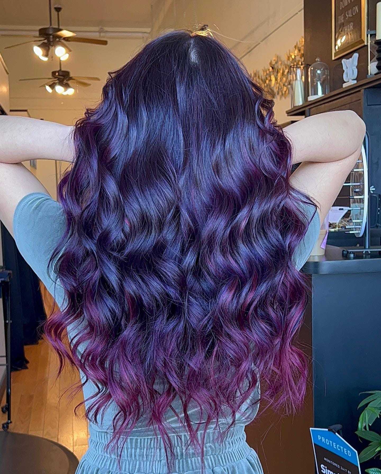 Wavy dark purple hair with highlights in a salon setting.